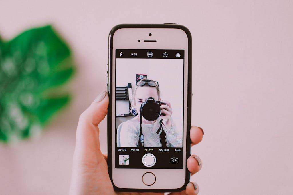 The photo of a person holding a DSLR camera on a phone monitor to illustrate taking real dental practice images